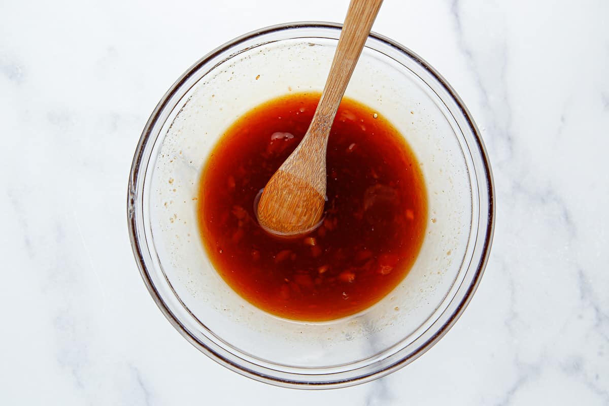 Sauce for honey sesame chicken in a glass bowl with a wood spoon.