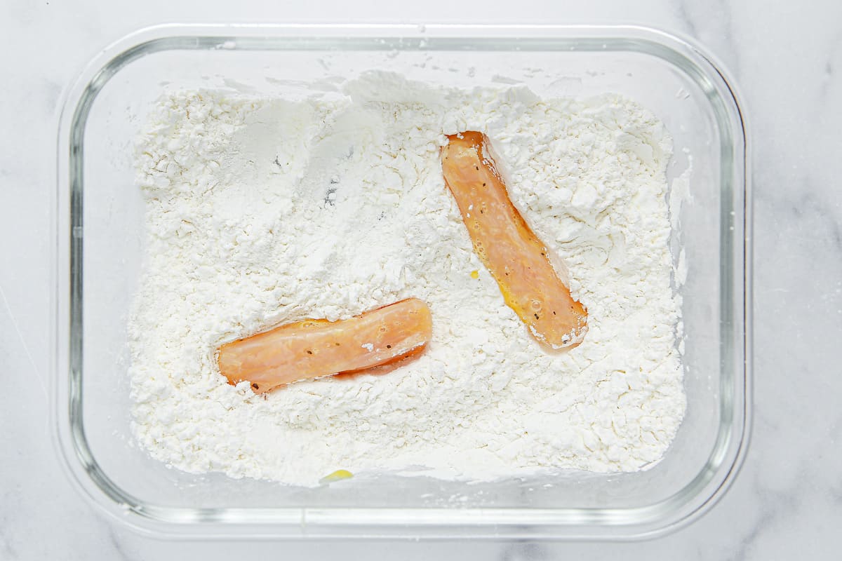 Chicken pieces in a container of cornstarch and flour.
