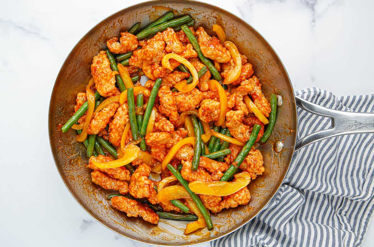 Chicken, green beans, bell pepper and sauce in a skillet.