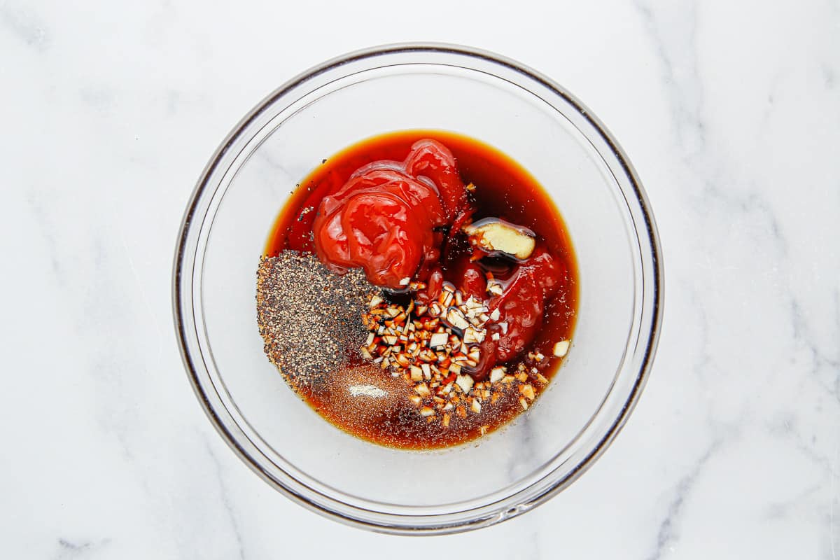 A glass bowl with all of the ingredients to make Korean BBQ sauce in it over a marble background.