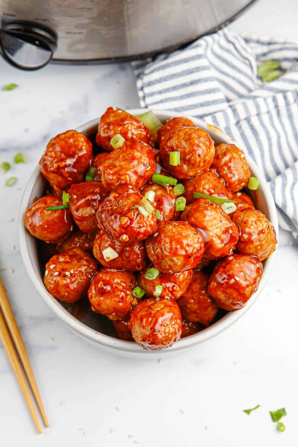 A white bowl full of Korean BBQ meatballs with a striped towel and chopsticks around it.