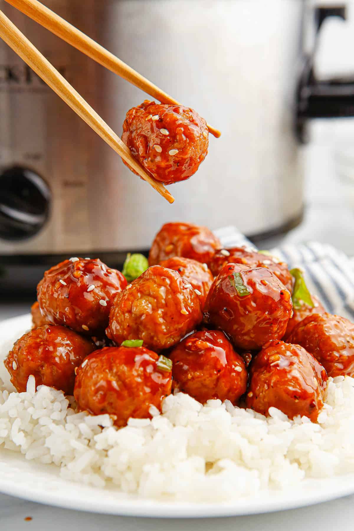 A single Korean barbecue meatball being help up with chopsticks over a bowl of more meatballs.