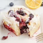 A lemon blueberry sweet roll on a plate with a fork with a piece cut out of it.