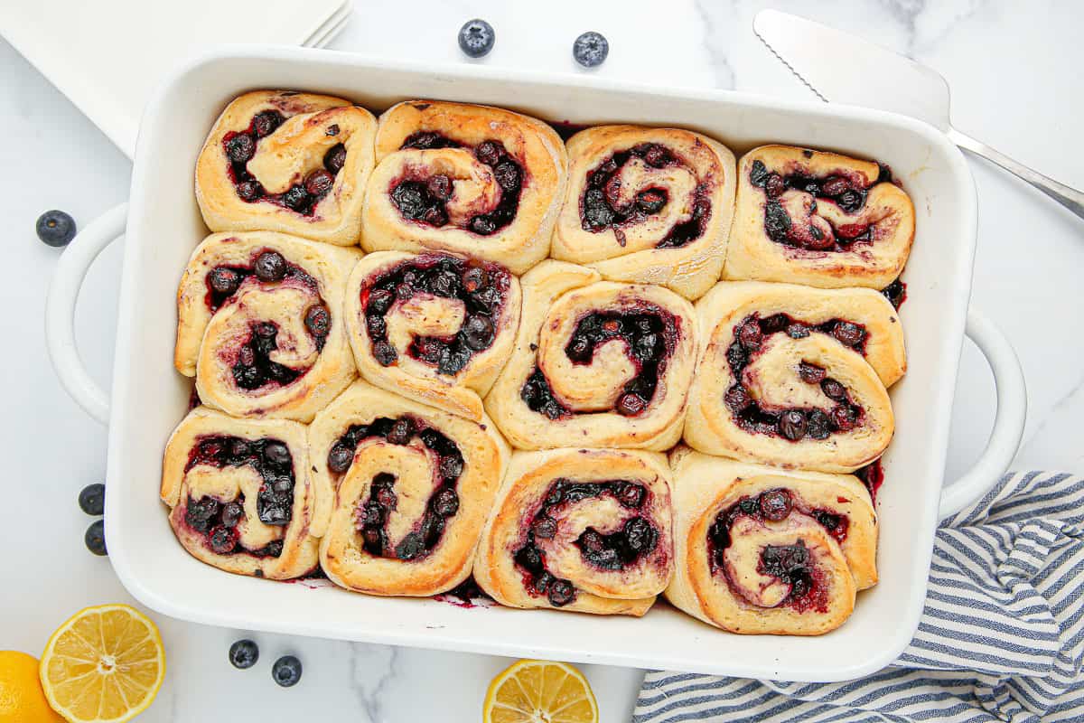 12 baked blueberry sweet rolls in a white baking dish.