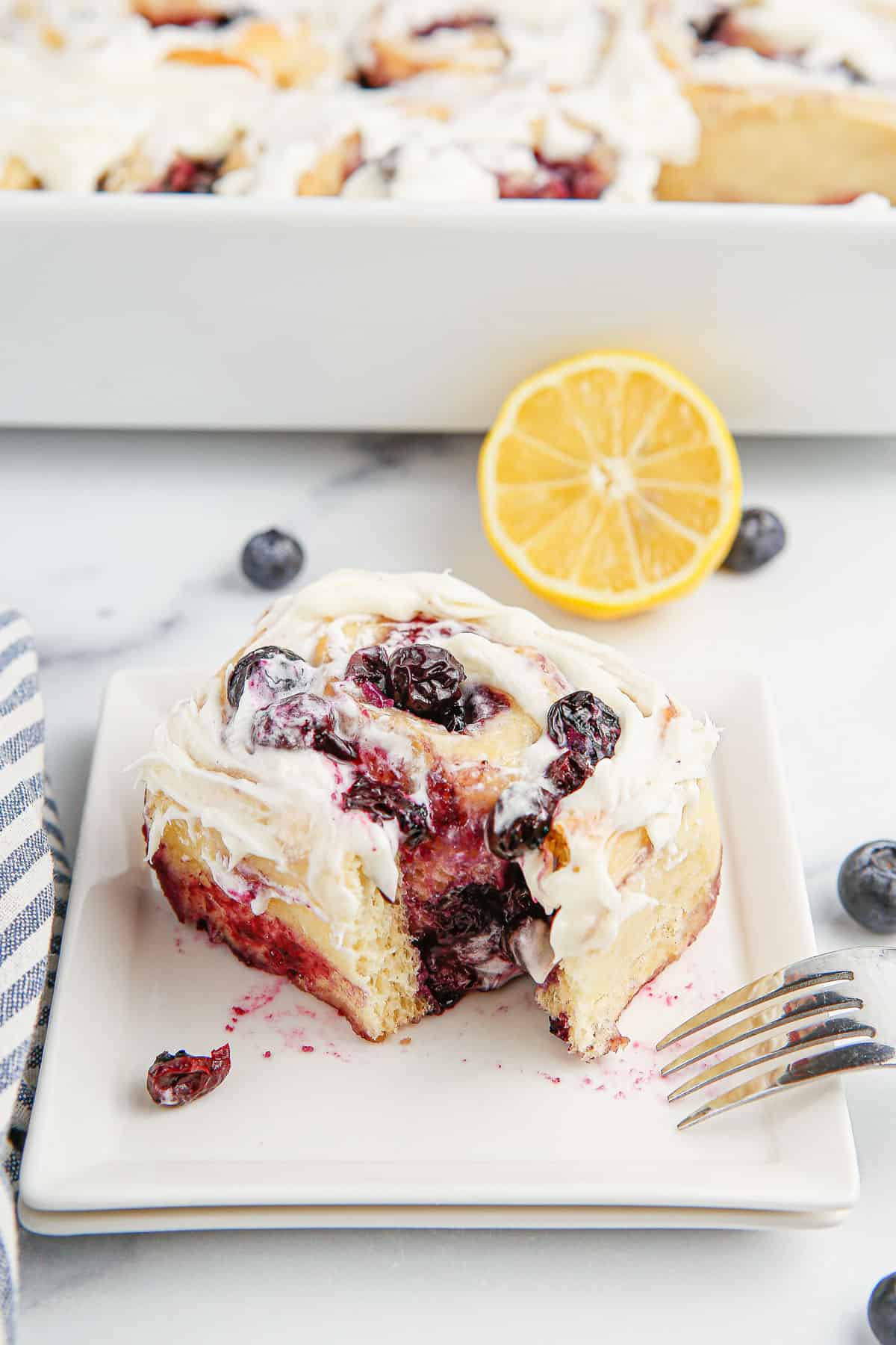 A. lemon blueberry sweet roll on a plate with a fork with a piece taken out of it.