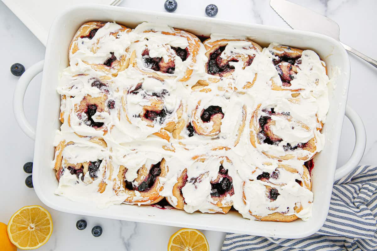 A baking dish of lemon blueberry sweet rolls topped with icing.