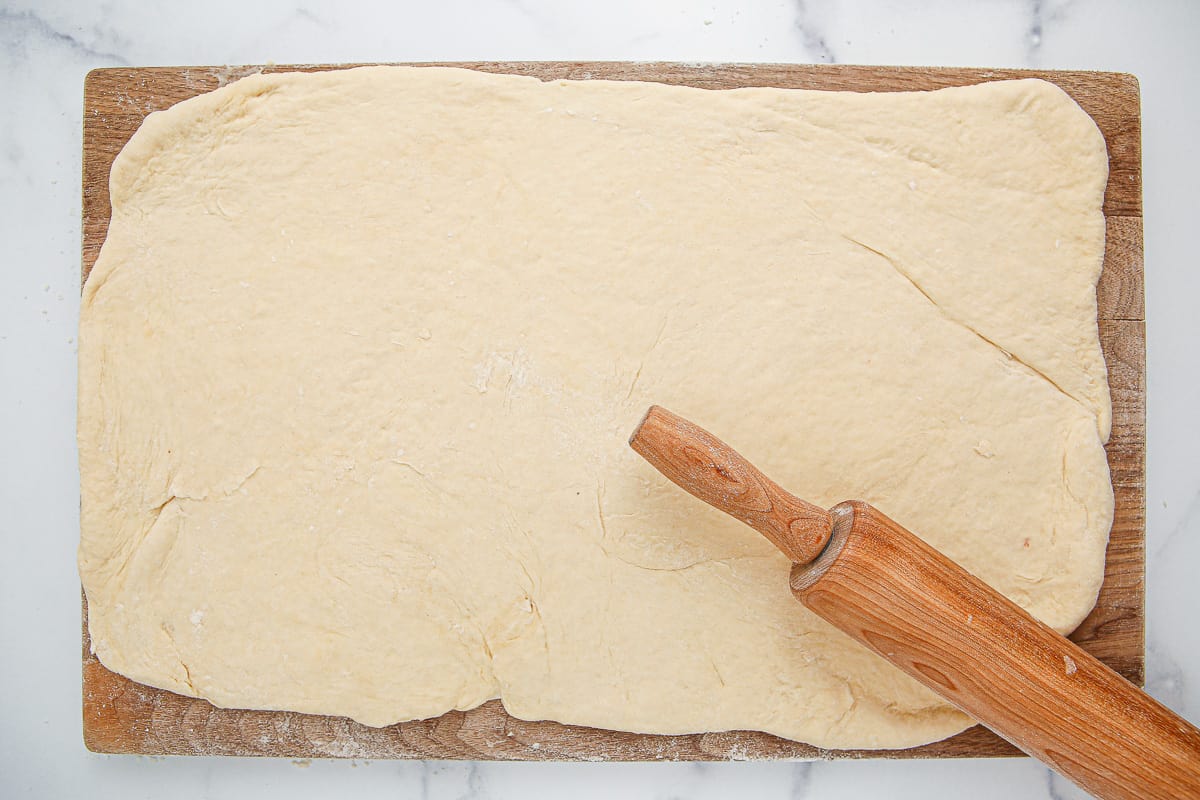 Dough rolled out onto a cutting board with a rolling pin on it.