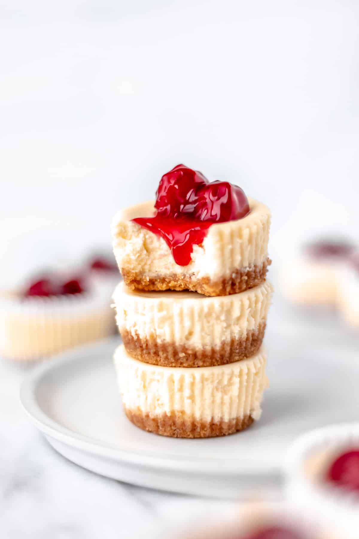 A stack of three mini cheesecake cupcakes with cherry pie filling on top.