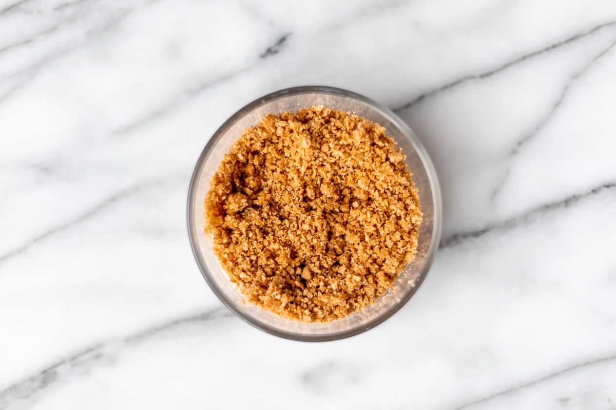 Wet graham cracker crumbs in a glass bowl on a marble background.