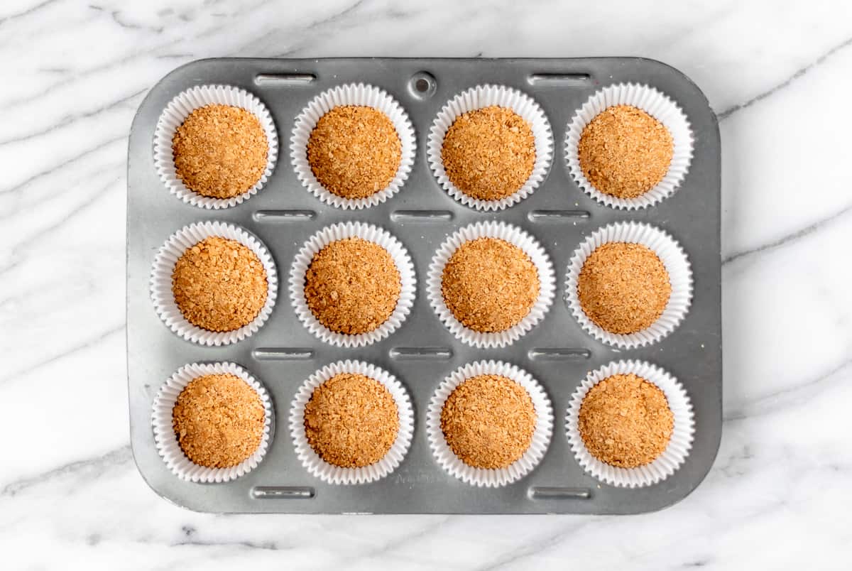 Graham cracker crust in the bottom of 12 cupcake liners in a pan.