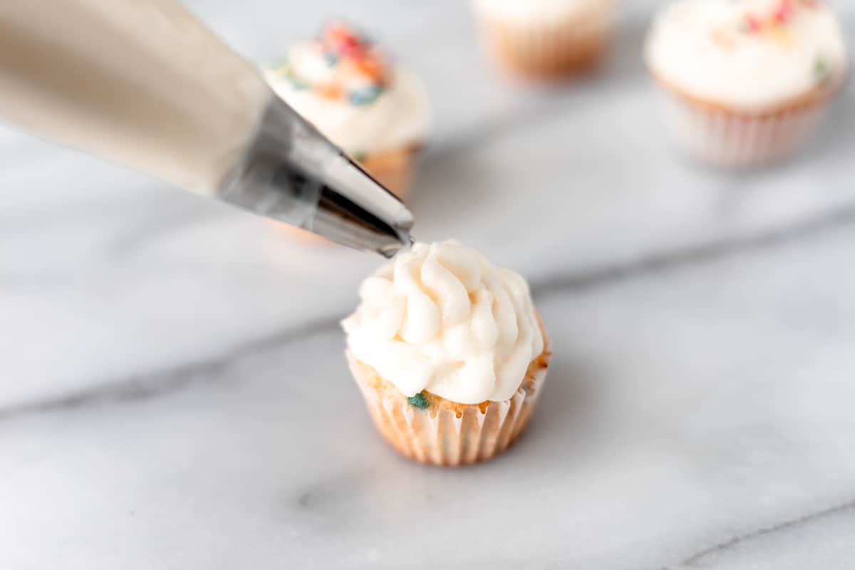 Frosting a mini cupcake with a piping bag and tip.