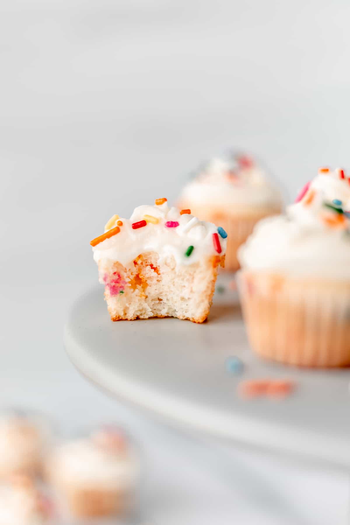 A mini sprinkle cupcake with a bite taken out of it on a cake stand.