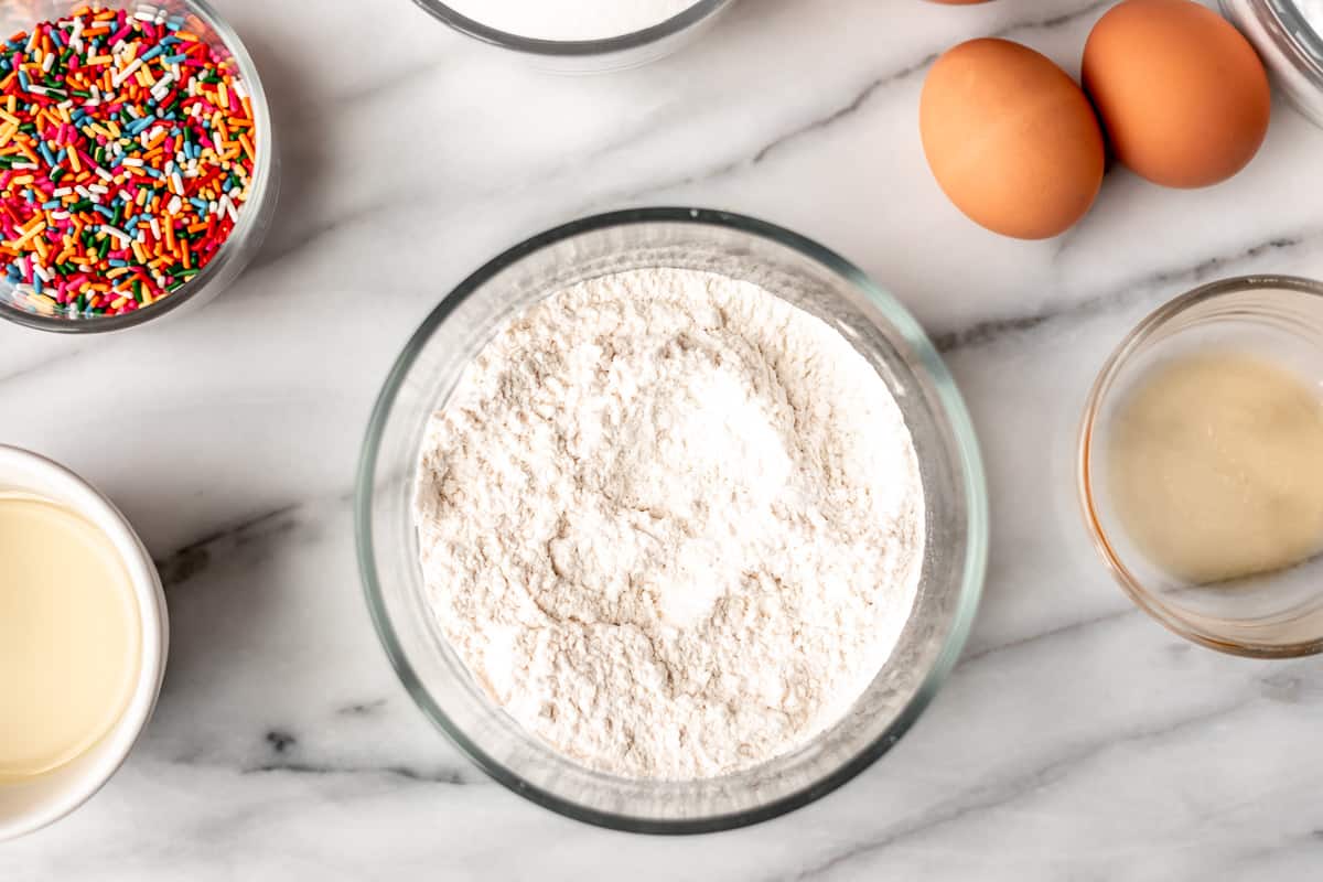 Flour, baking powder and salt combined in a small glass bowl with other ingredients around it.