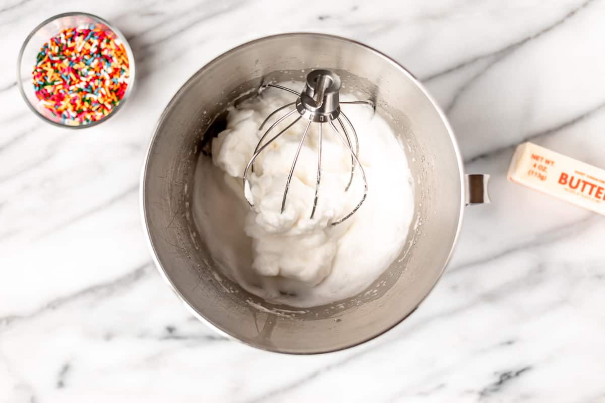 Whipped egg whites in a silver mixing bowl with a whisk attachment.