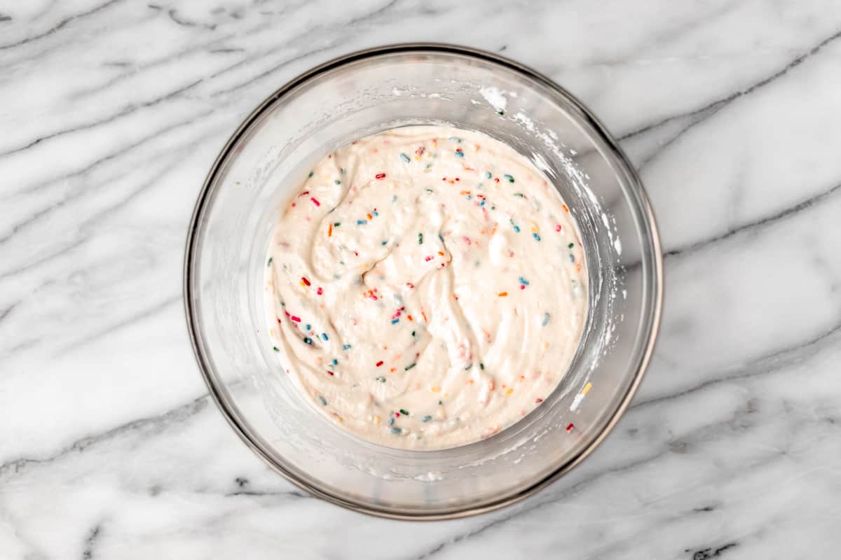 Cake batter with sprinkles mixed into it in a large glass bowl.