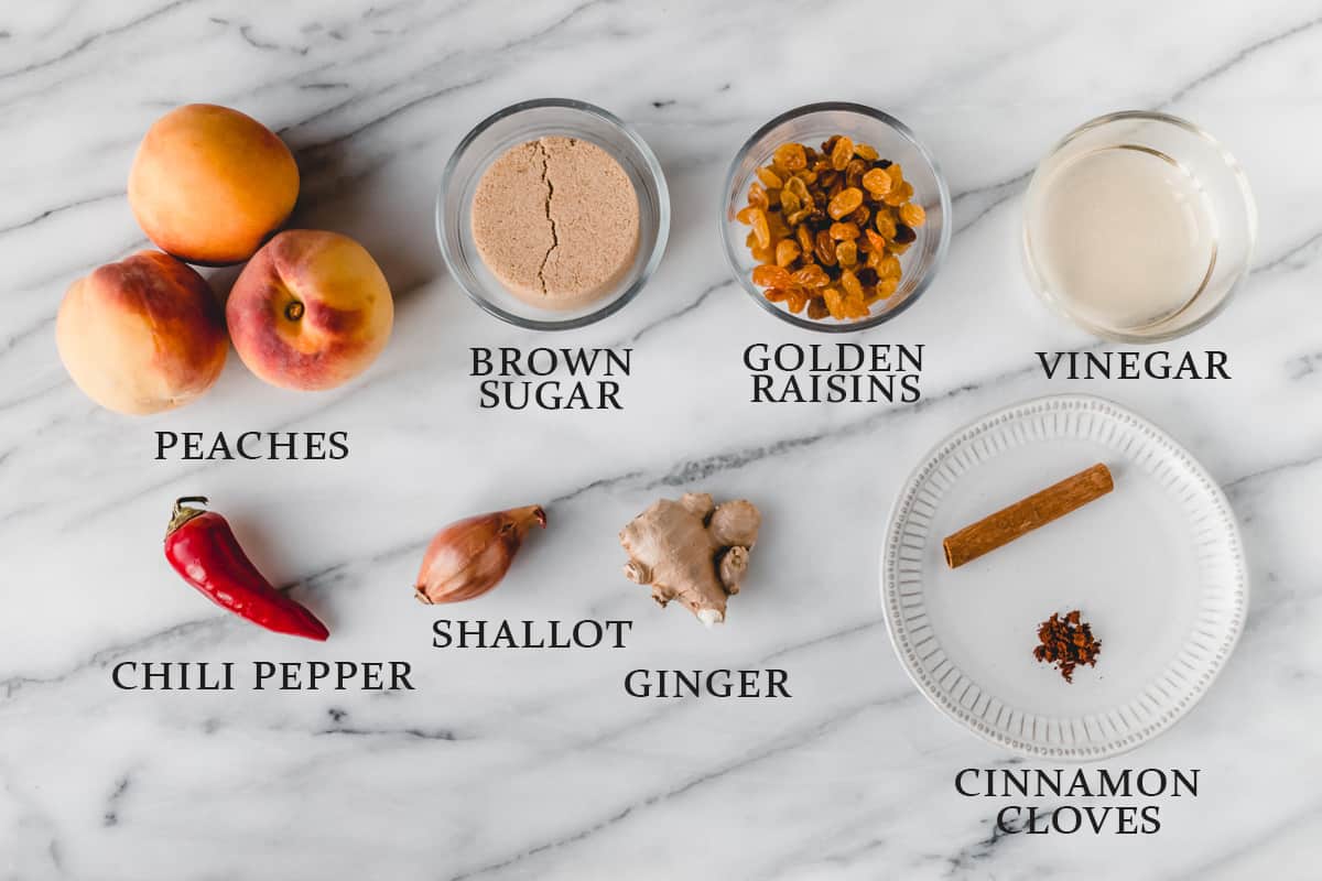 Ingredients to make peach chutney on a marble background with text overlay.