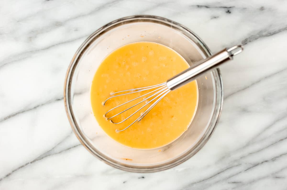 whisked eggs, cream and cheddar cheese in a glass bowl with a metal whisk.