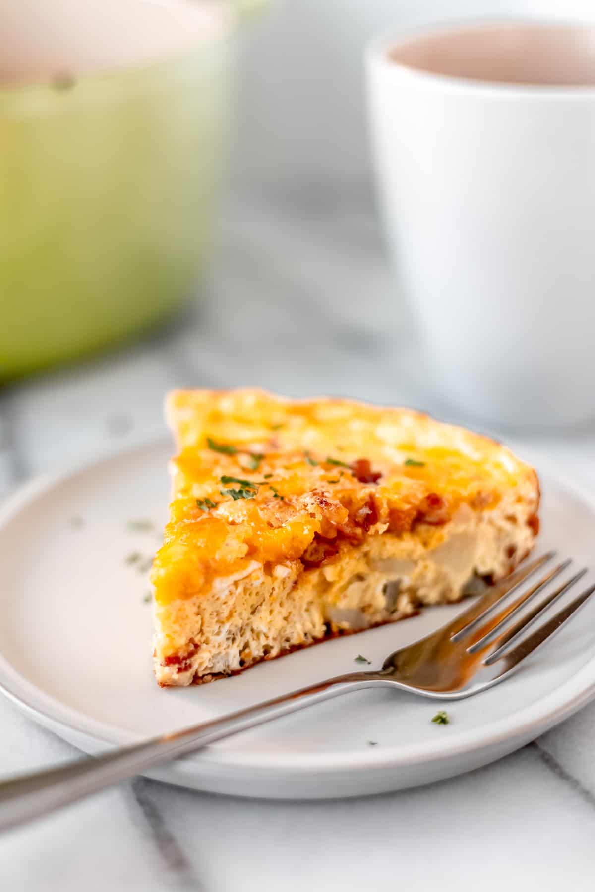 A slice of potato frittata on a small white plate with a fork.