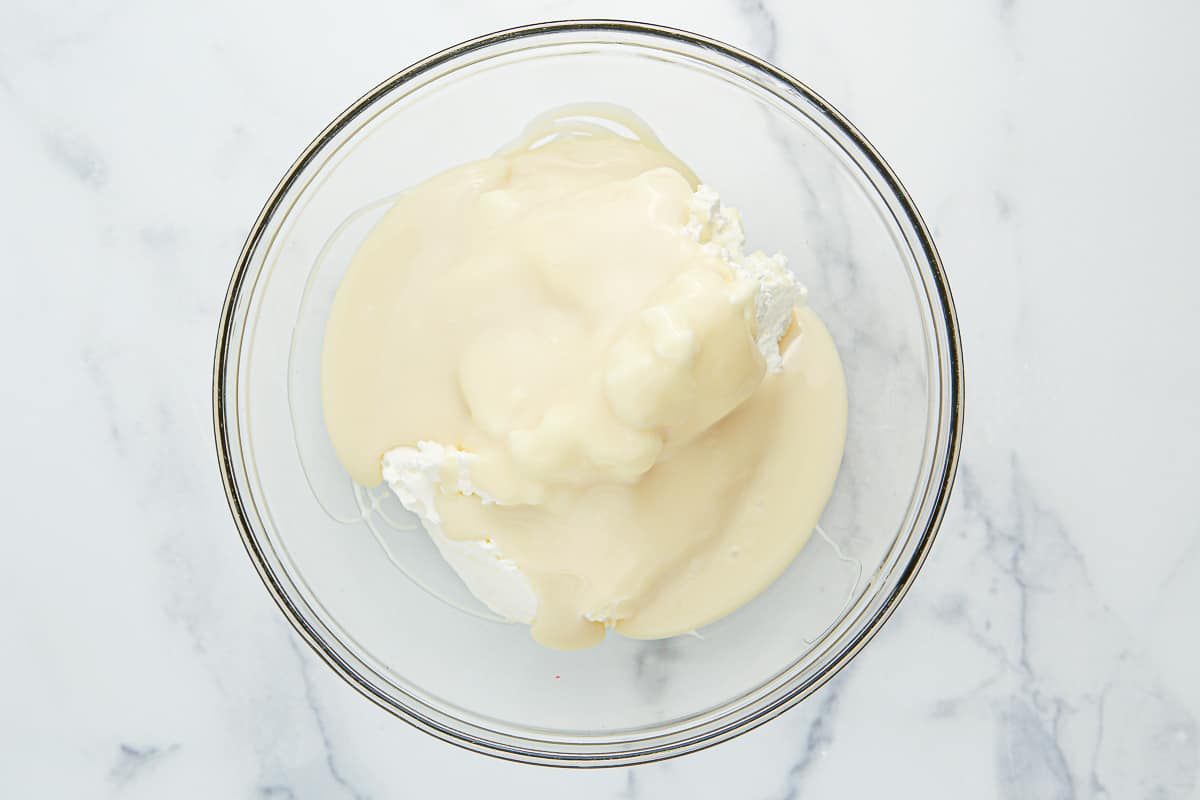 Whipped heavy cream with sweetened condensed milk in a glass bowl.