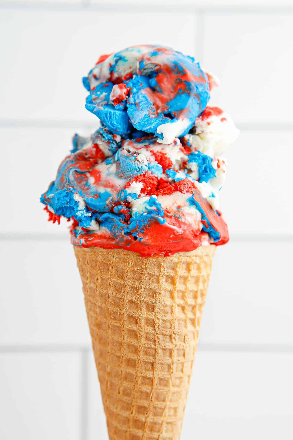 An ice cream cone with 2 scoops of red, white and blue ice cream in it.