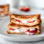 Close up of two halves of Strawberry French Toast stacked on top of each other on a white plate with a second plate blurred in the background.