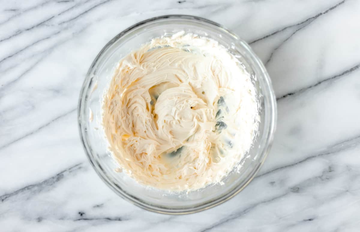Whipped cream cheese in a glass bowl over a marble background.