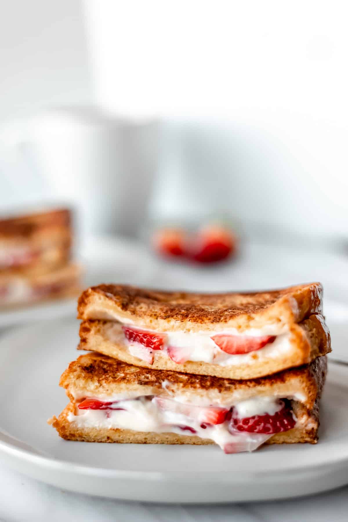 Close up of two halves of Strawberry French Toast stacked on top of each other on a white plate with a second plate blurred in the background.