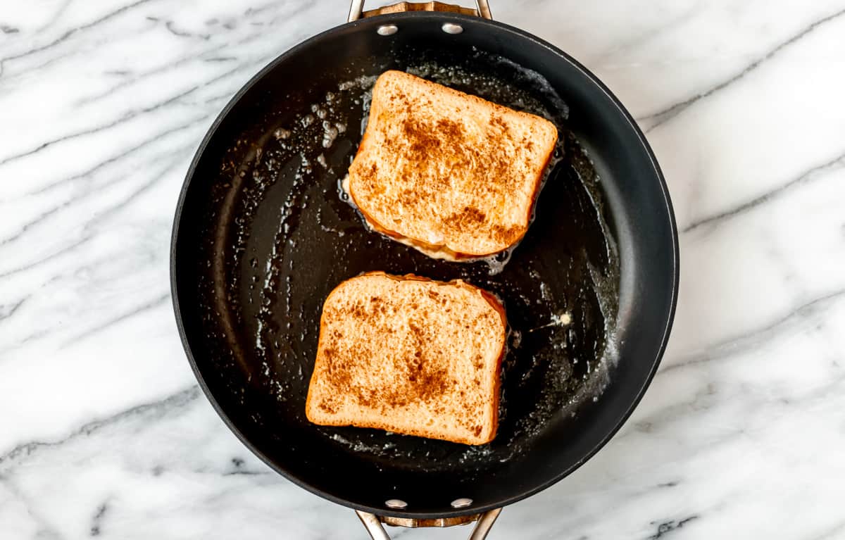 French toast topped with cinnamon cooking in a black skillet.