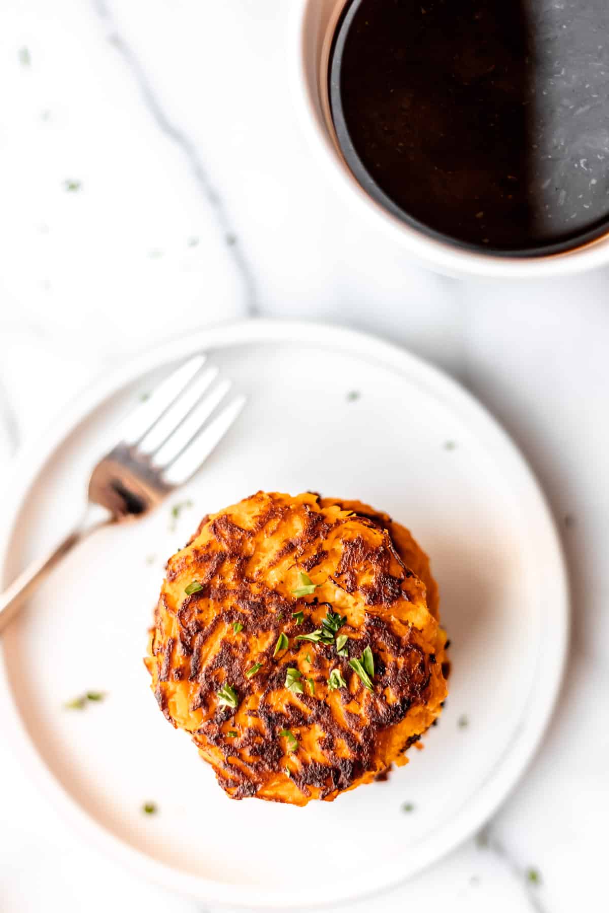Overhead of sweet potato hash browns on a white plate with a fork and a cup of coffee off to the side.