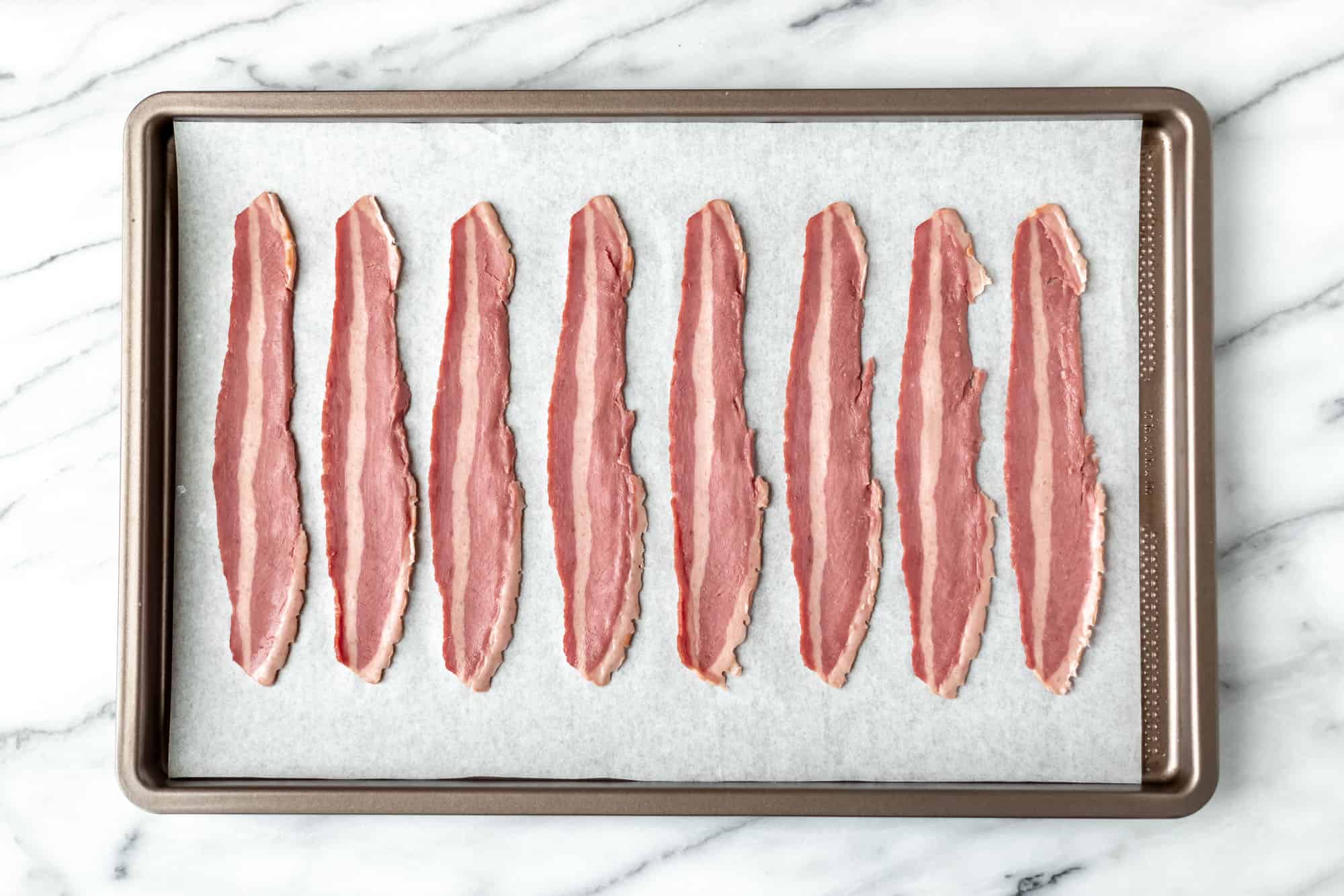 Uncooked turkey bacon strips on a parchment paper lined baking sheet.