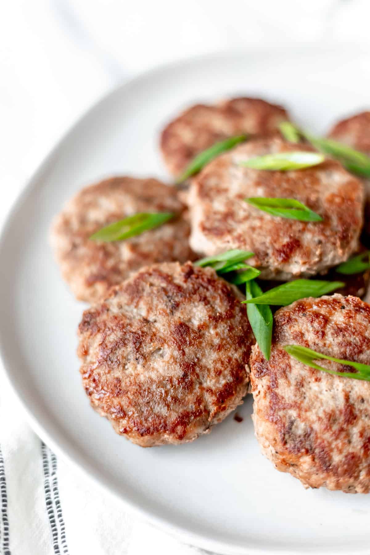 Overhead of turkey sausage patties stacked on top of each other and garnished with sliced green onions on a white plate.