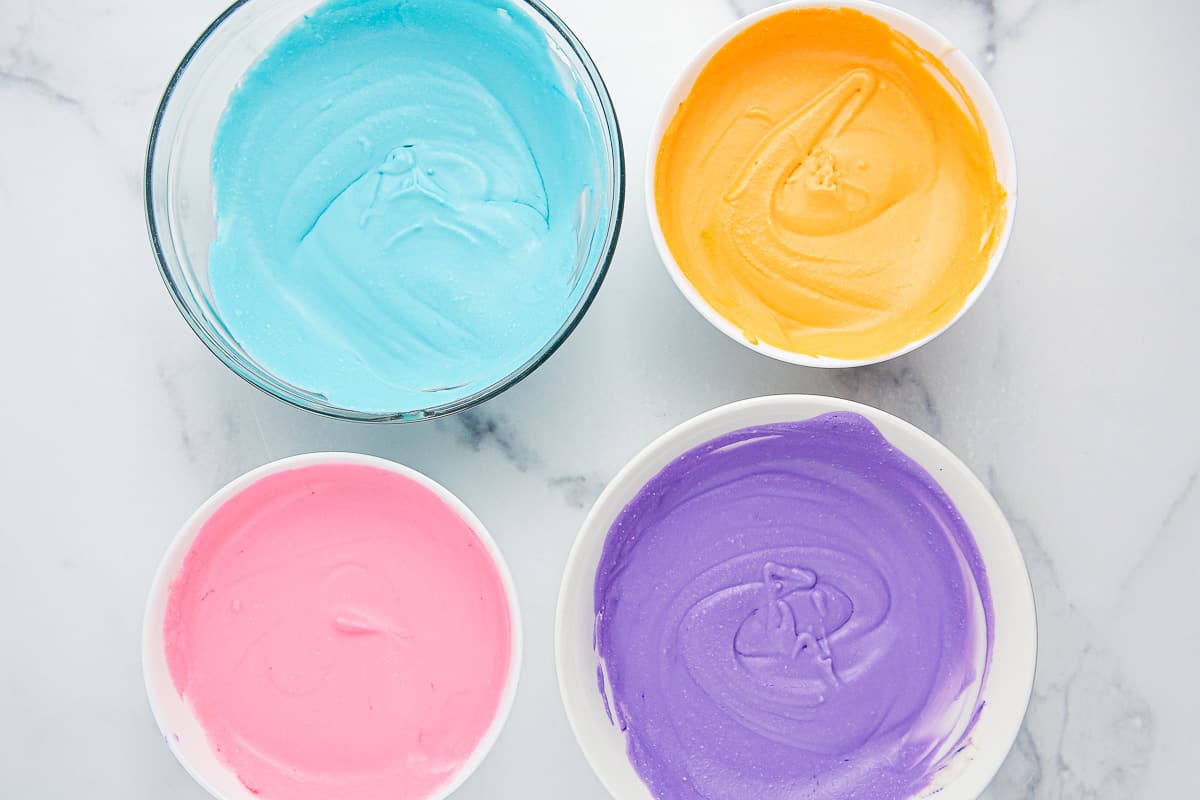 Four bowls of colored ice cream mixture - blue, orange, pink and purple.
