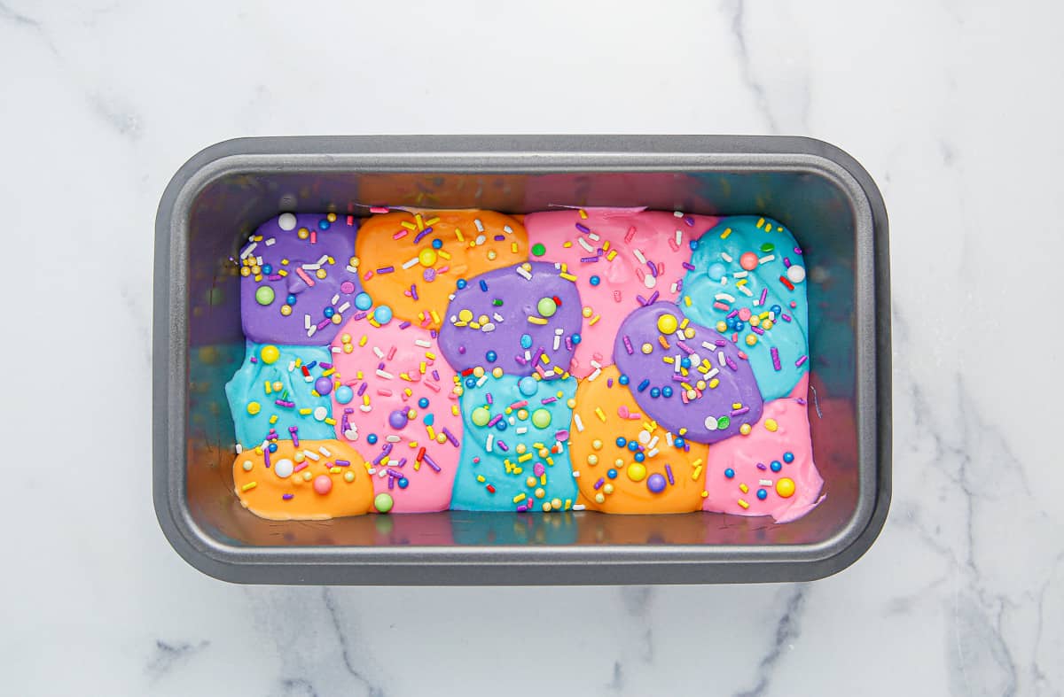 Multi-colored ice cream in a loaf pan topped with pastel sprinkles.