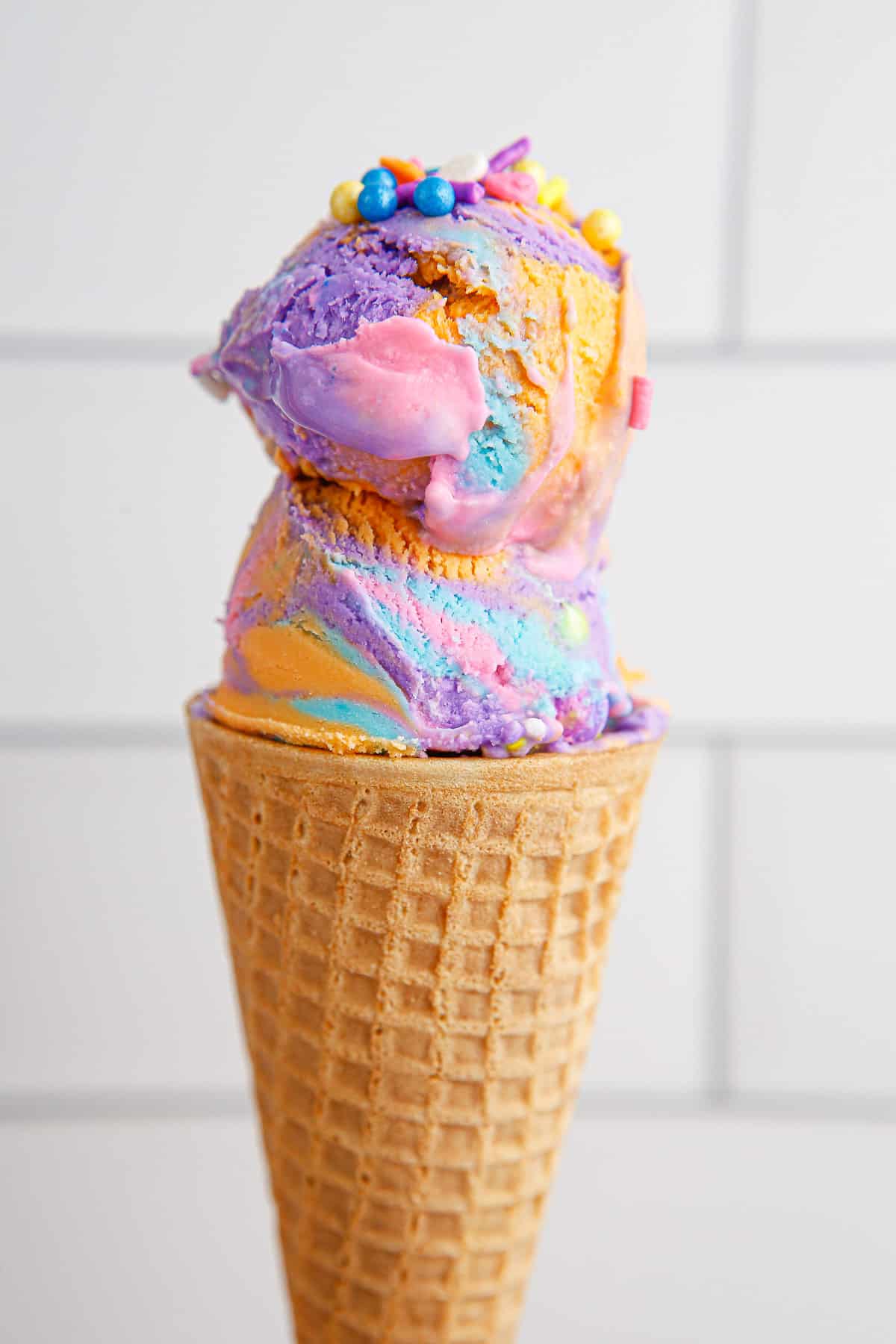 Close up of pink, orange, purple and blue unicorn ice cream in an ice cream cone.