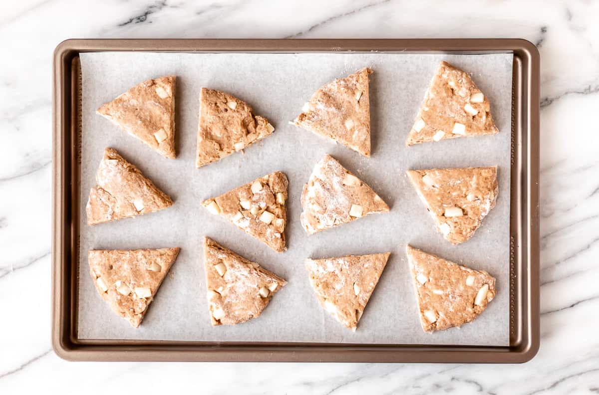 12 unbaked apple cinnamon scones on a parchment paper lined baking sheet.