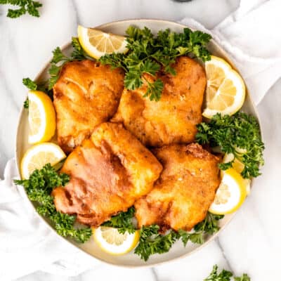 Beer battered cod fillets on a plate with parsley and lemon slices.