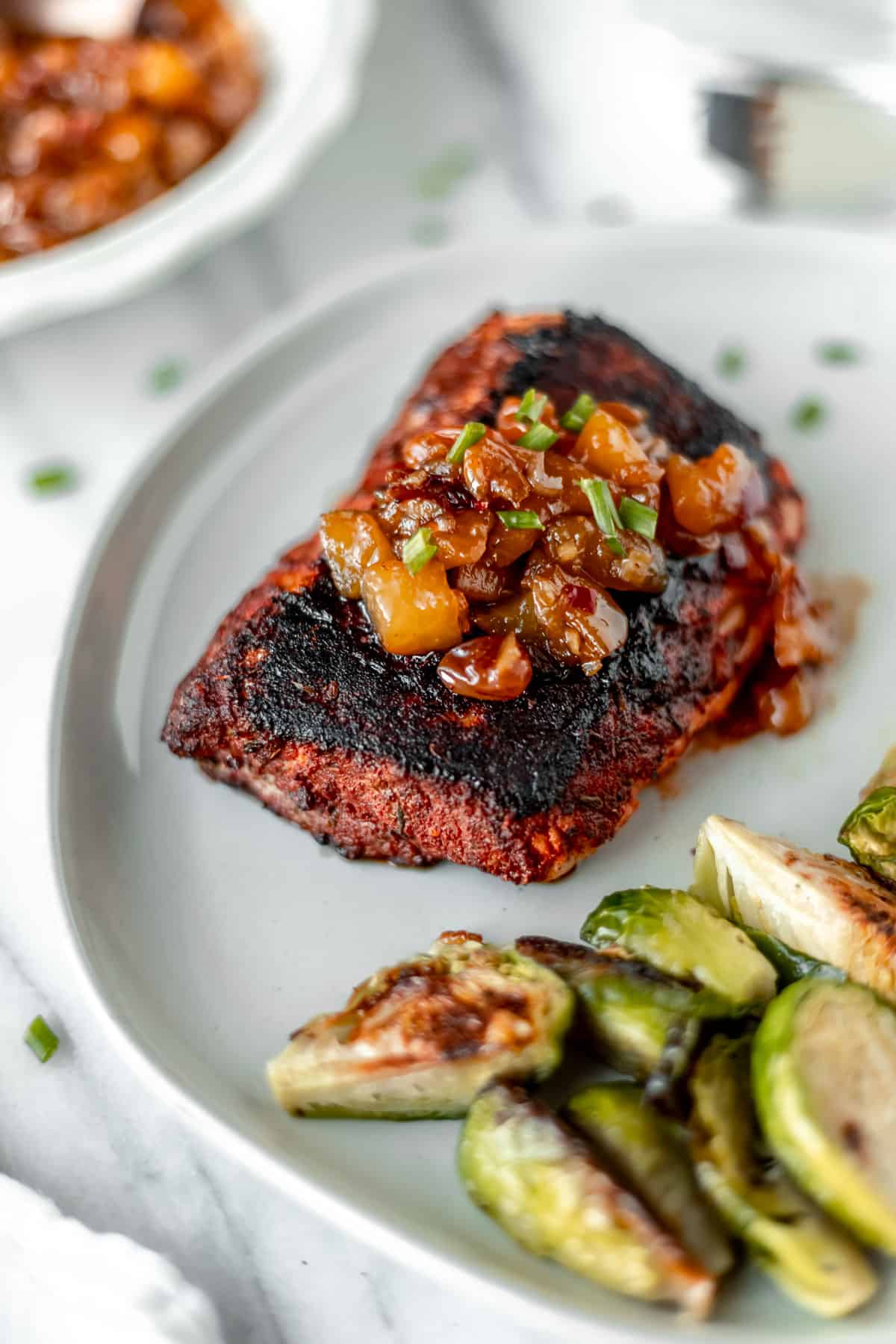 Peach chutney on top of blackened fish on a white plate with brussels sprouts.
