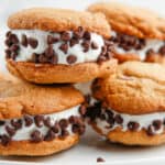 A plate of four chocolate chip cookie ice cream sandwiches with mini chocolate chips on the ice cream.