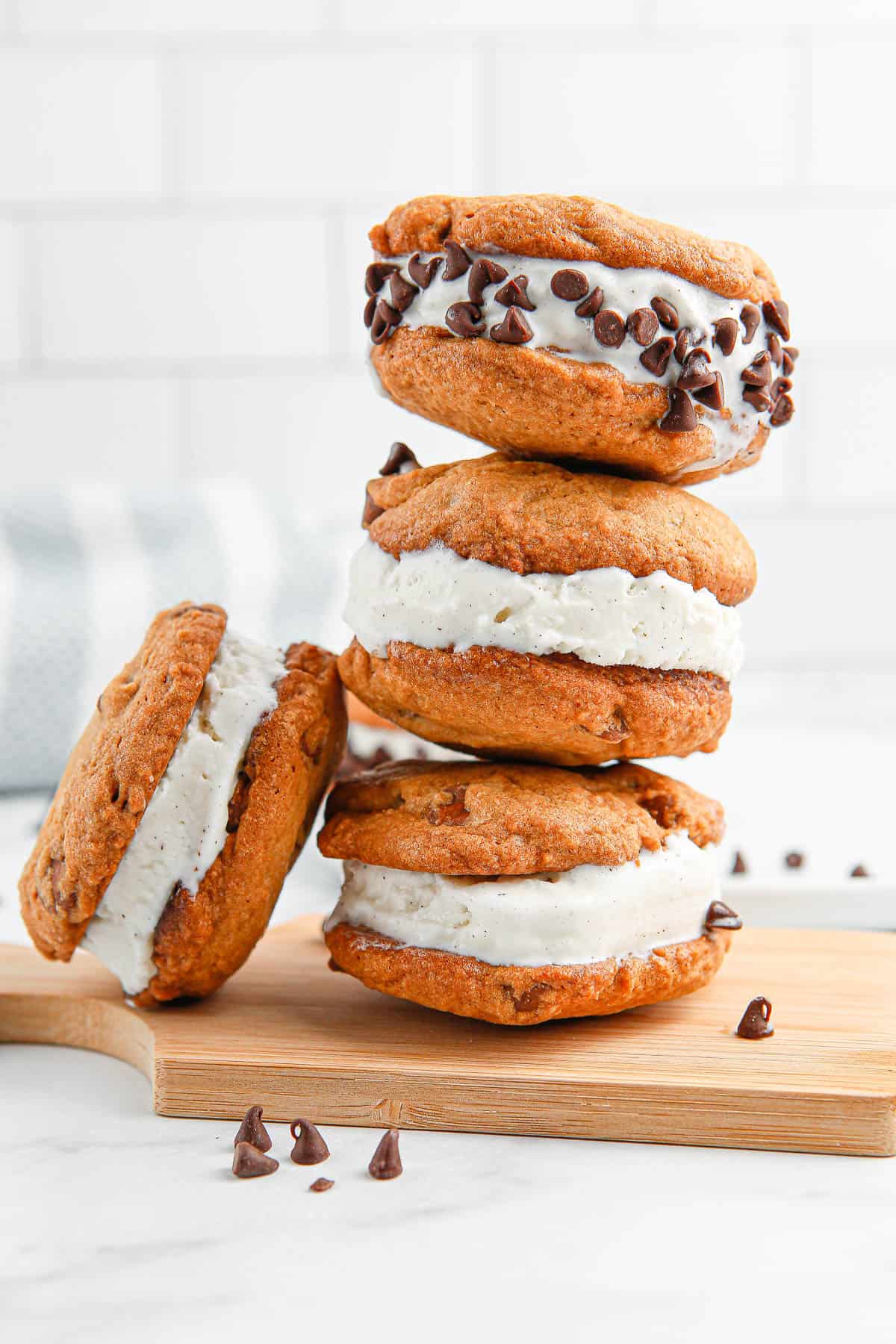 A stack of three chocolate chip cookie ice cream sandwiches with mini chocolate chips stuck to the ice cream on the top one.