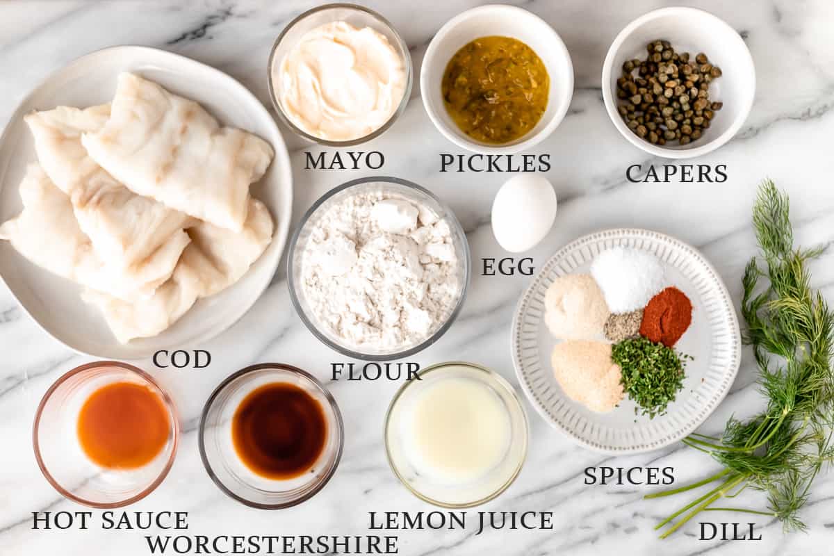 Ingredients to make a cod sandwich and homemade tartar sauce on a marble background with text overlay.