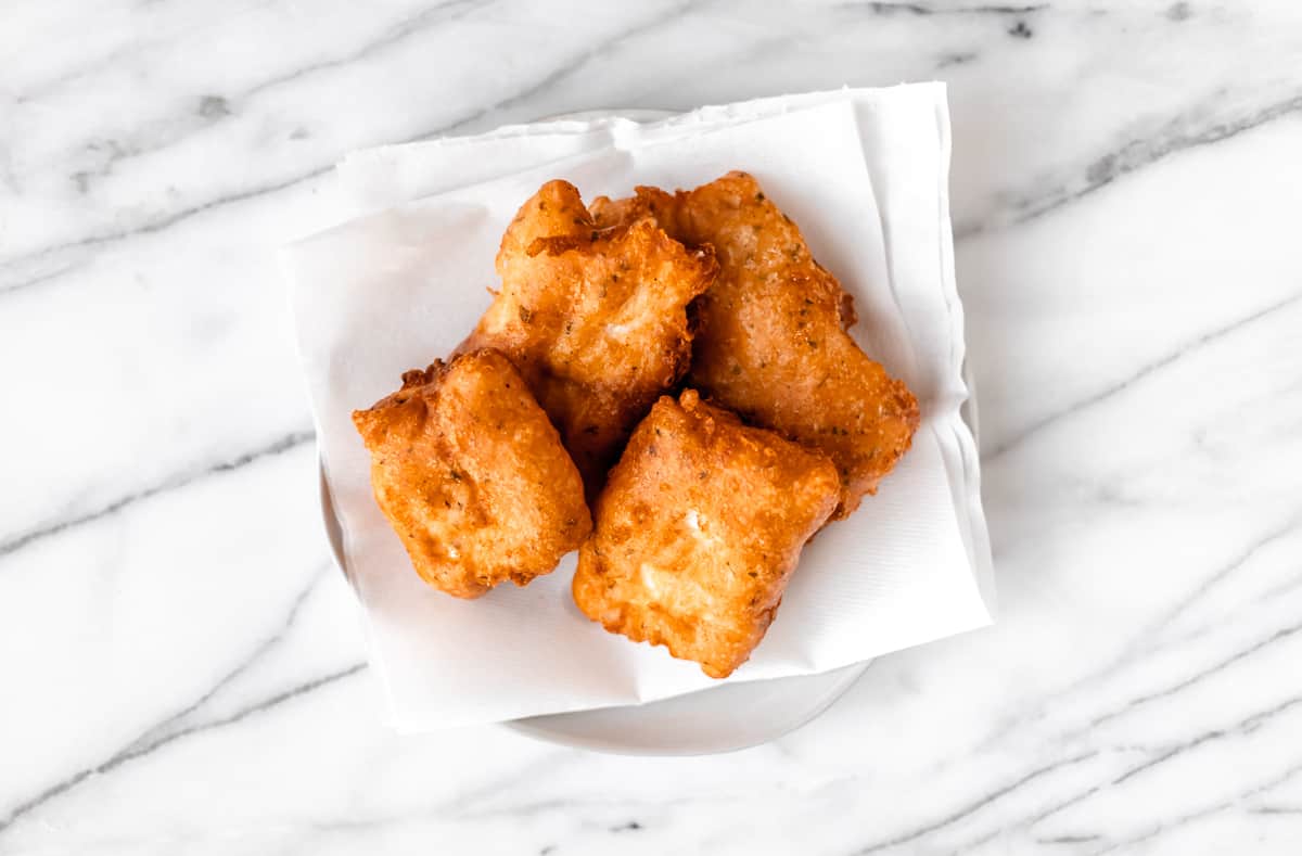 Beer battered cod fillets on a paper towel-lined plate over a marble background.