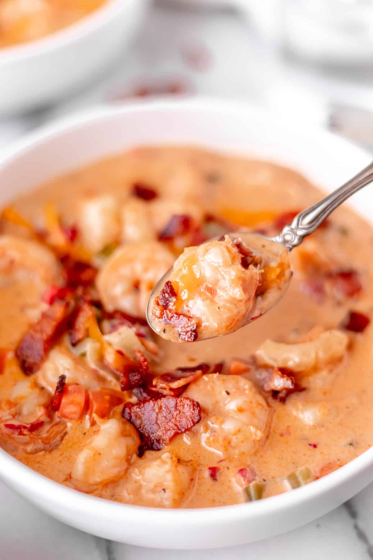 A spoon lifting up a bite of creamy shrimp chowder over the bowl of more soup.
