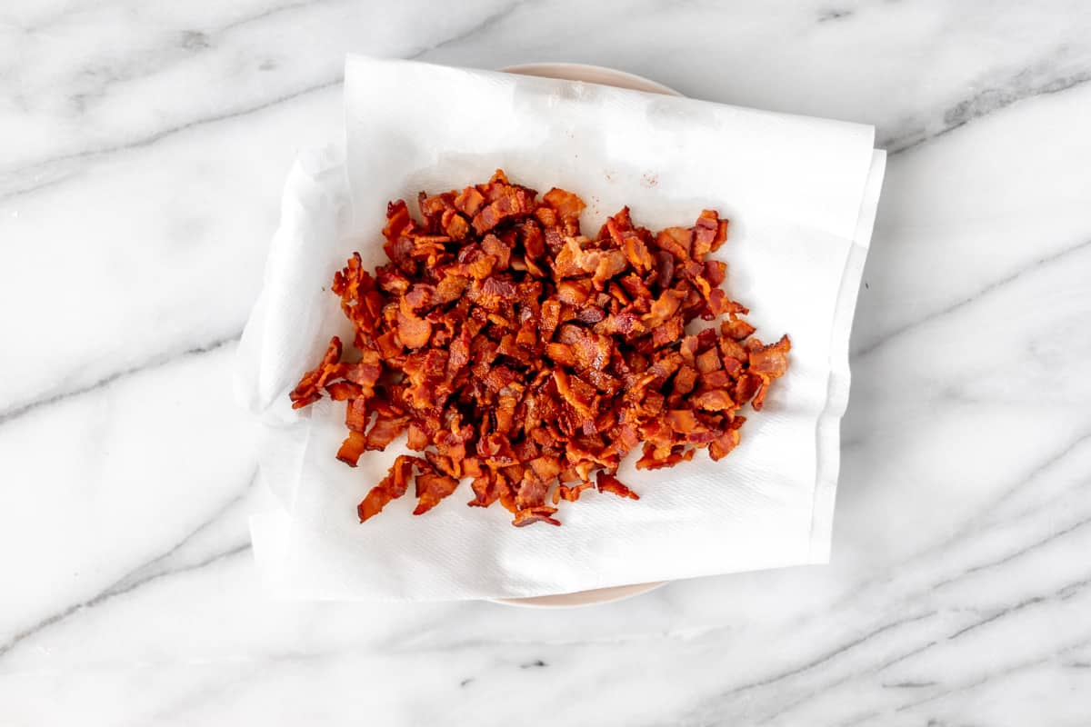 Crisp, crumbled bacon on a paper towel-lined plate on a marble background.