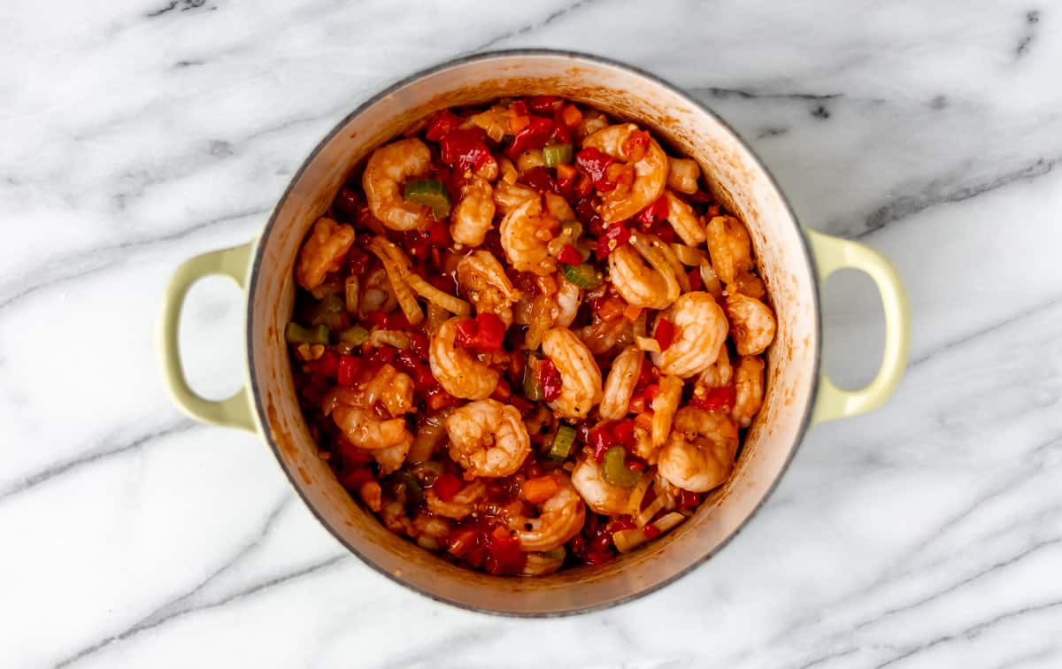 Shrimp and vegetables in a Dutch oven over a marble background.