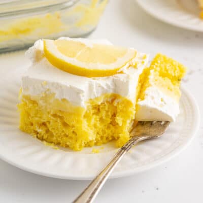 A slice of lemon poke cake with a bite taken out on a fork next to the cake.