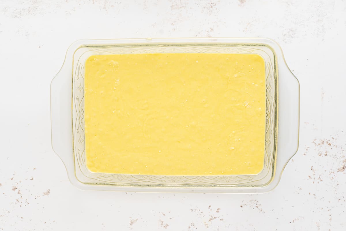 Lemon cake batter in a rectangular cake pan on a white surface.