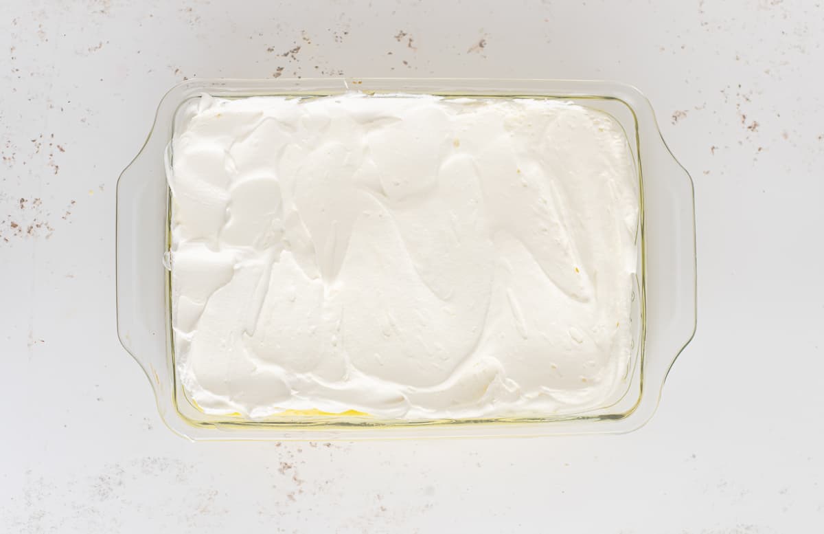 Overhead of cool whip spread on top of a rectangular cake.