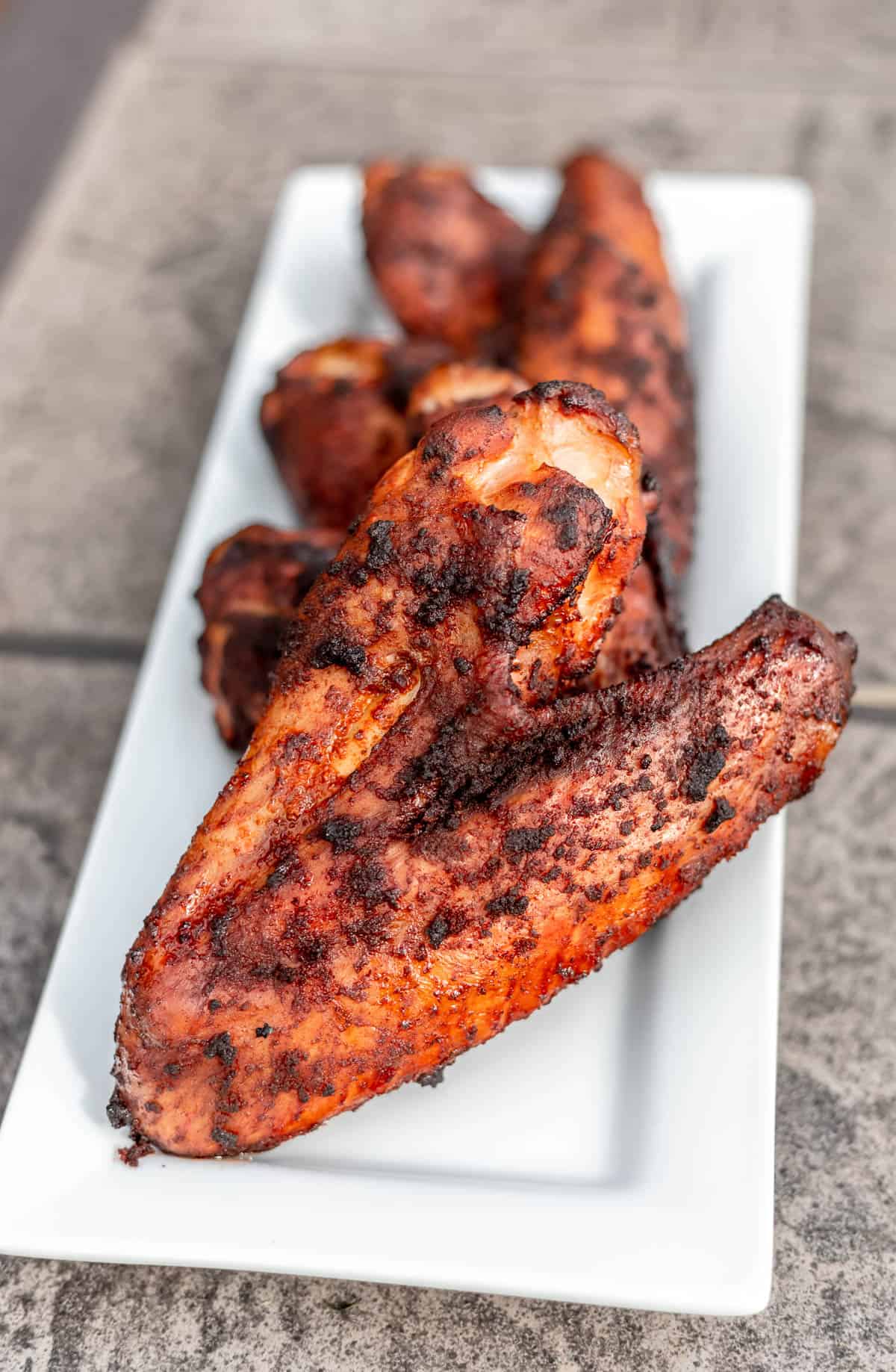 Smoked turkey wings on a white serving plate on a tan table.