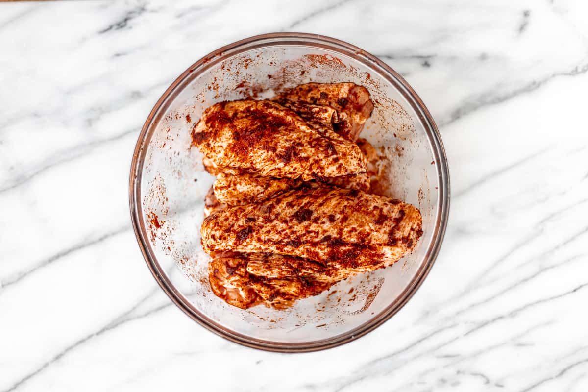 Turkey wings coated in spiced in a glass bowl over a marble background.