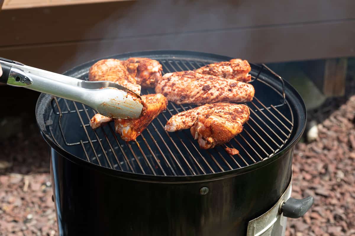 Turkey wings being placed onto a smoker.